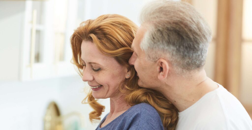 A mature couple embracing warmly in front of a window, representing emotional repair and reconnection in a relationship.